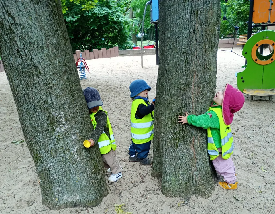 Drei Kinder in Warnwesten umarmen im Park Baumstämme