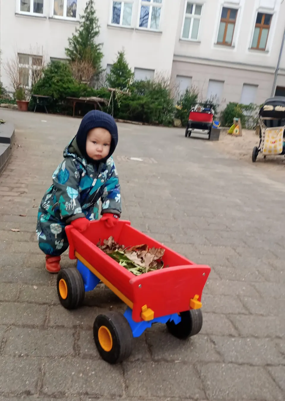 Ein Kind zieht einen roten Bollerwagen über den Hof
