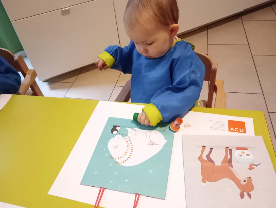 Ein Kind im blauen Malkittel malt an einem gelben Tisch