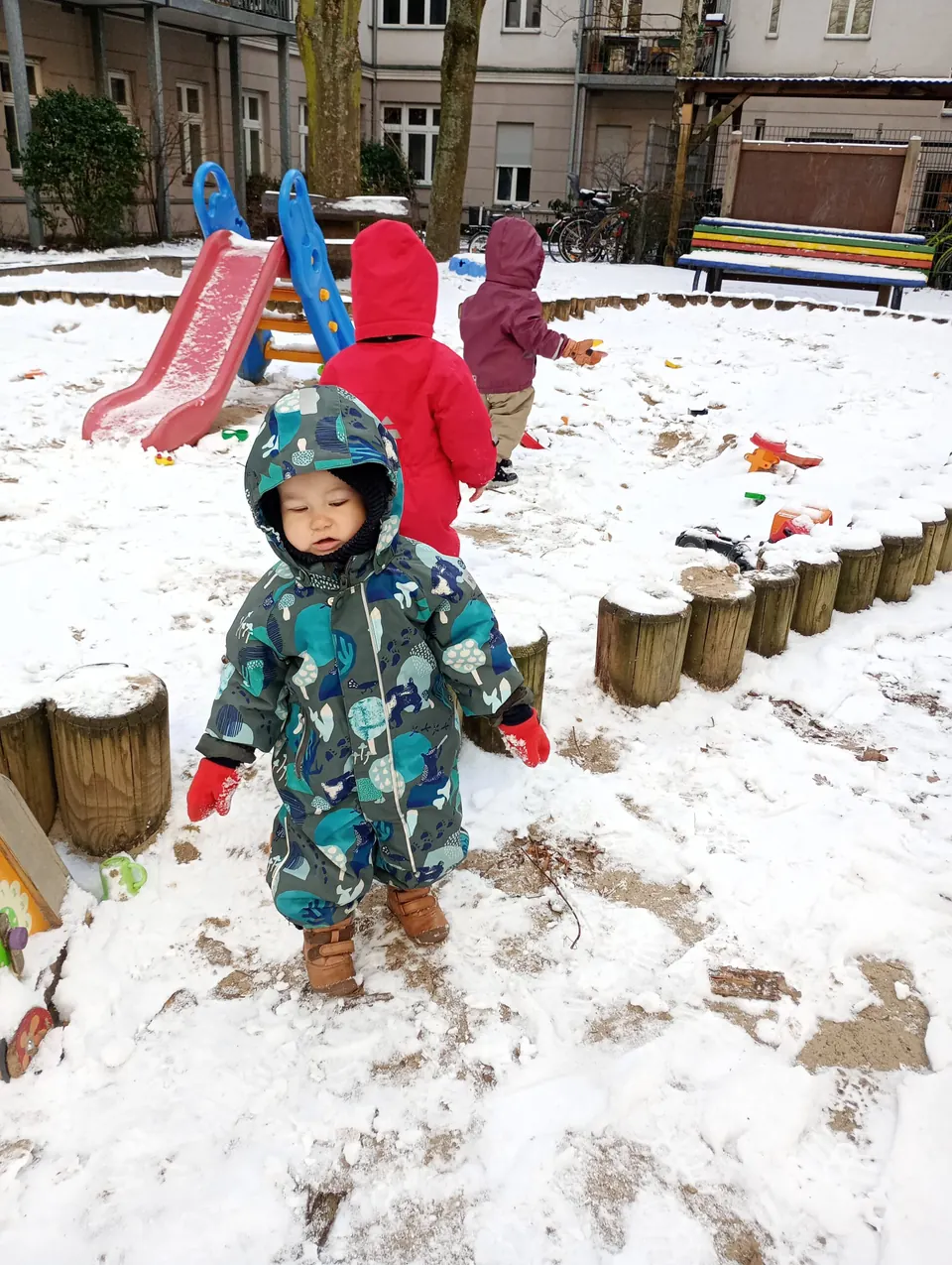 Ein Kind in blauem Overall im verschneiten Sandkasten